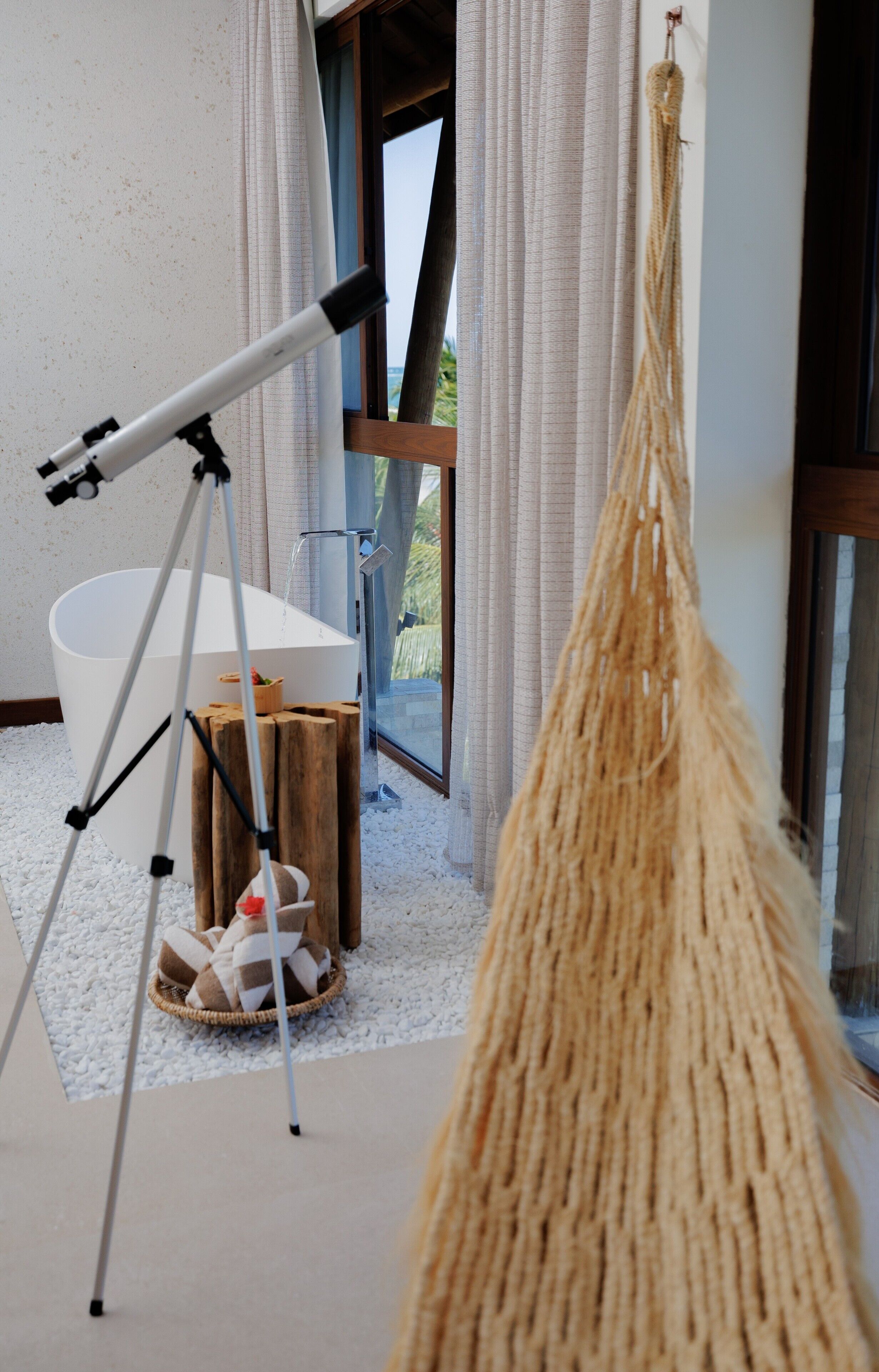 Uma casa de banho moderna com uma banheira grande, um telescópio e um macramé pendurado no teto.