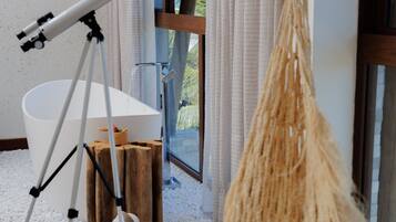 Uma casa de banho moderna com uma banheira grande, um telescópio e um macramé pendurado no teto.