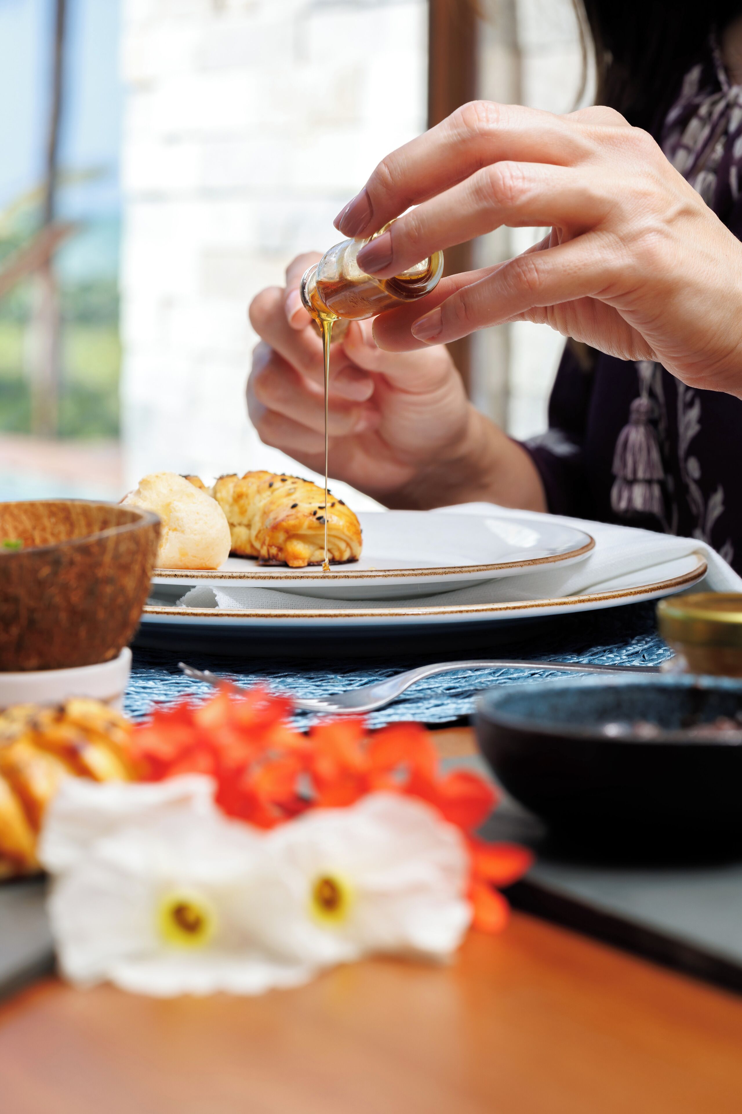 A person pouring a liquid from a small container onto a plate with food items.