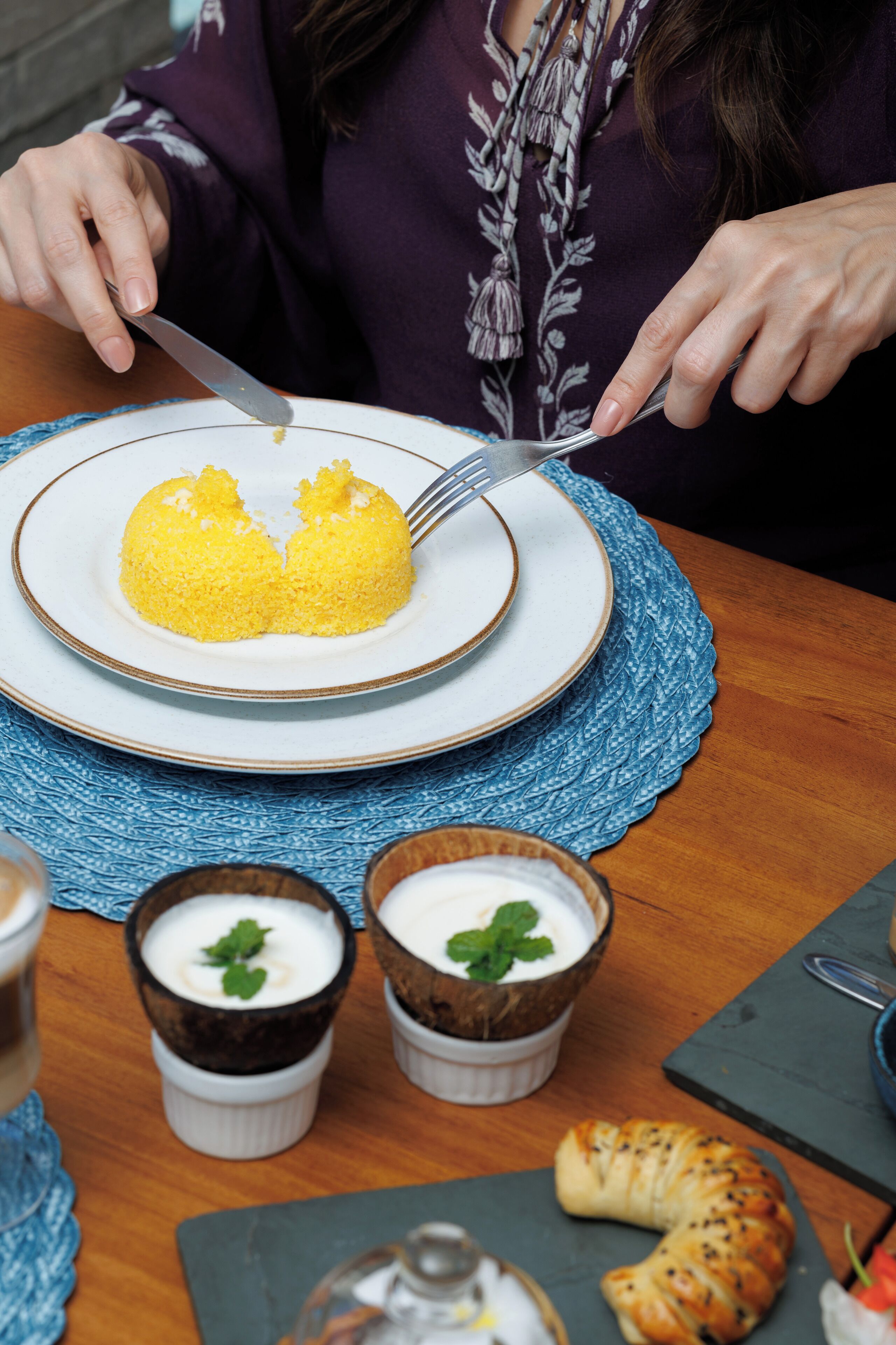 A dining table with a plate of yellow food, two small cups with a white creamy substance, and a croissant.