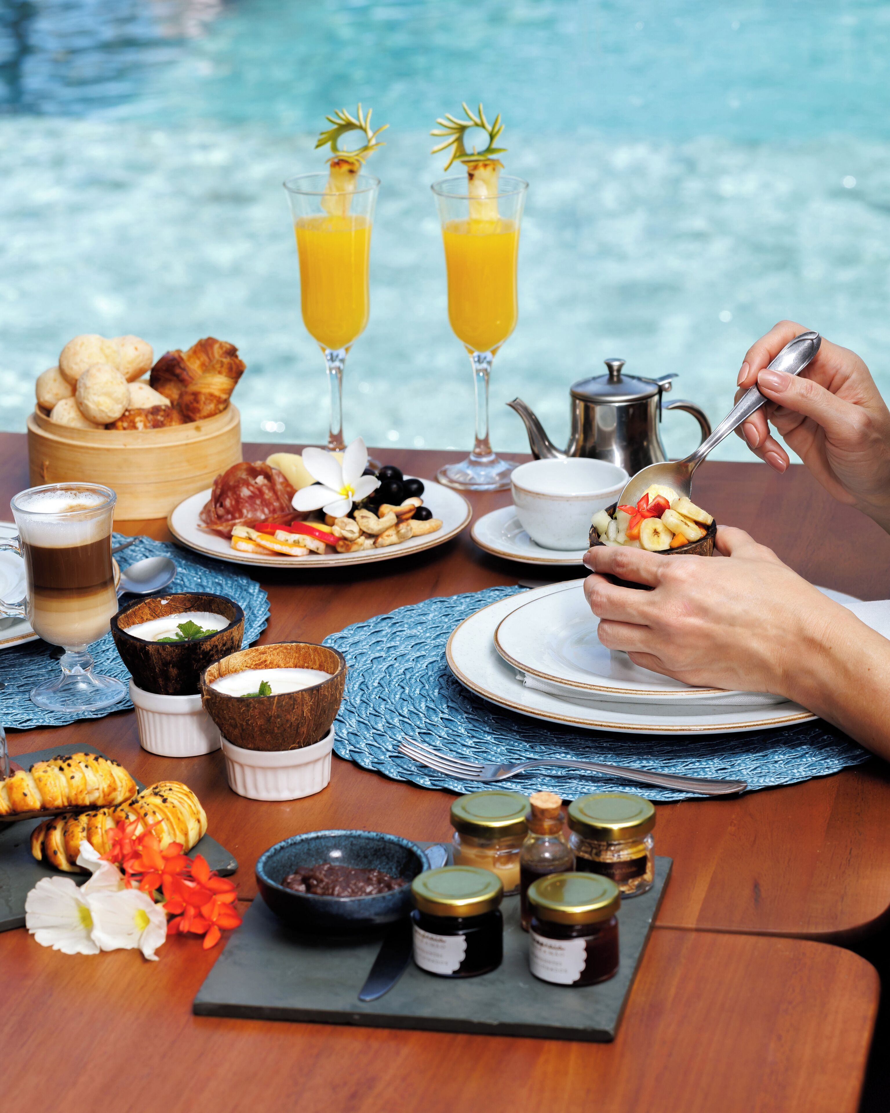 A breakfast setting with a pool view, including croissants, pastries, fruit, and beverages.