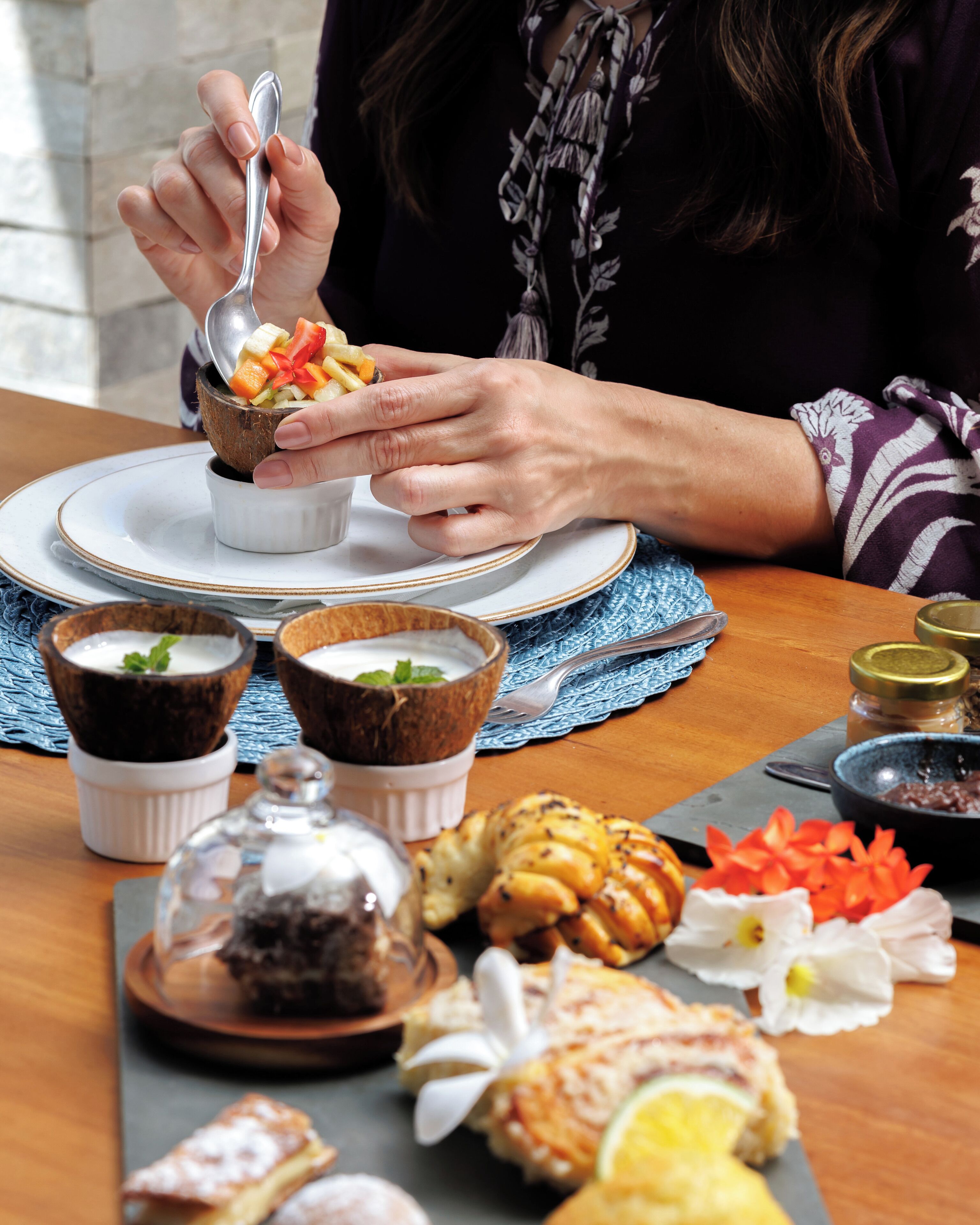 A person serving food from a bowl, with various dishes and pastries on a table.