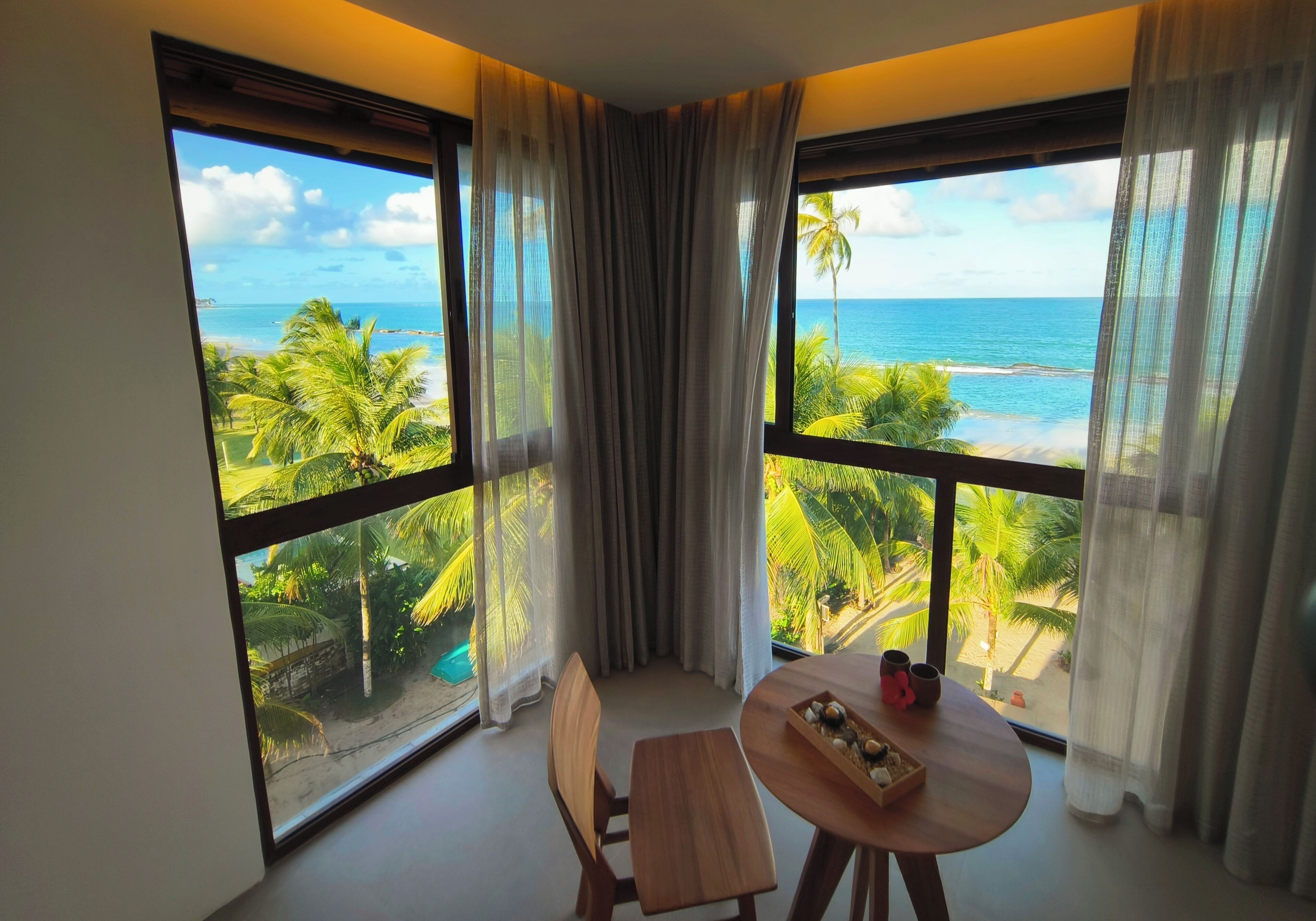 A room with a large window overlooking a beach, a wooden table with a tray of snacks, and a chair.