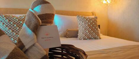 Ein Hotelzimmer mit Bett, Kissen, Decke, einem Korb und einer Karte mit der Aufschrift 'Almaria Boutique Hotel'.