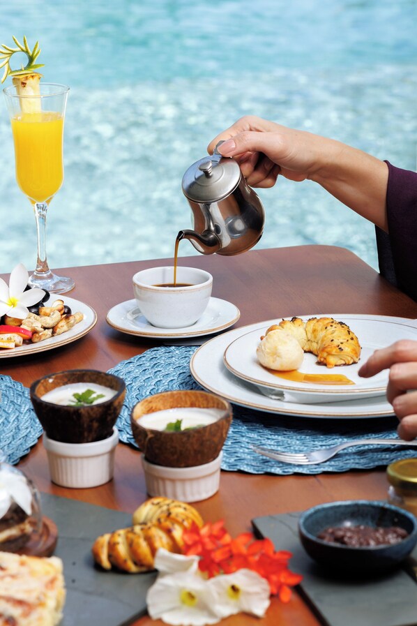 Et morgenbord med en croissant, et glas appelsinjuice og kaffe, der hældes i en kop.