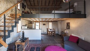 A loft-style living space with a wooden staircase, a dining area, and a sofa with a red cushion. - Chic and spacious self-catered loft cottage, ideal for work or romantic getaway (SOYAUX)