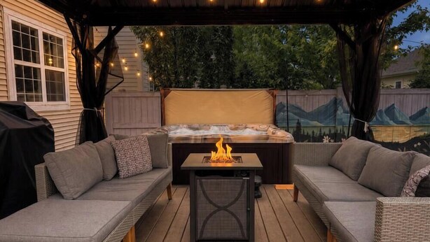 Un patio al aire libre con jacuzzi, zona de estar y luces colgantes.