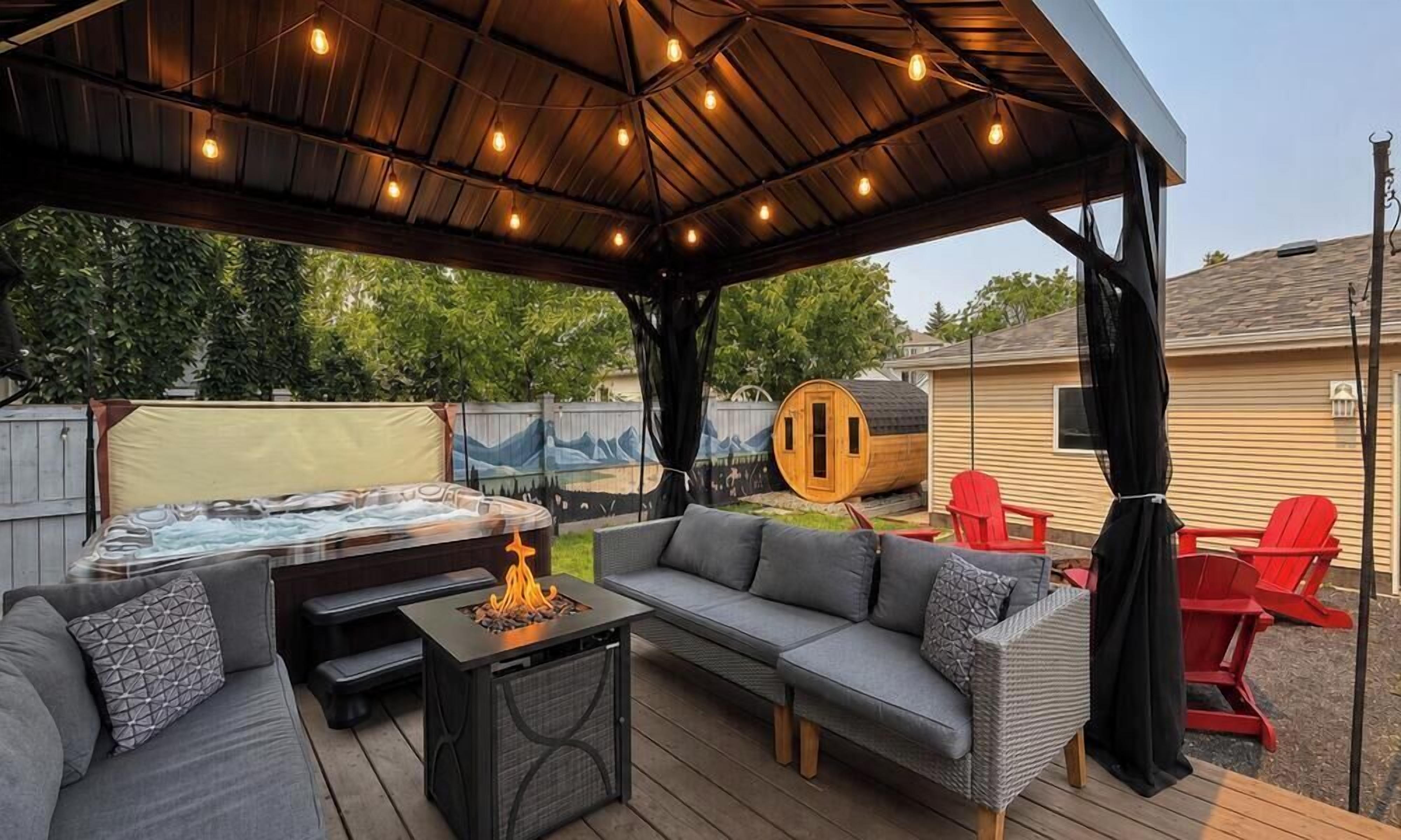 An outdoor patio with a covered seating area, a hot tub, and red Adirondack chairs.