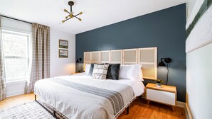 Un dormitorio con cama, mesitas de noche, lámpara, ventana con cortinas y una lámpara en el techo.