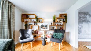 Una sala de estar con dos sillones, una mesa de centro y una estantería llena de libros y objetos decorativos.