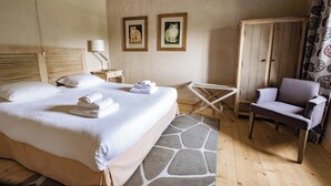 Un dormitorio con una cama grande, una silla de madera, una mesita pequeña y dos cuadros en la pared.