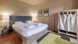 A neatly made bed with white linens and towels, a bedside lamp, and a framed picture on the wall. - Ground level two-bedroom gîte with gated yard. Ideal for young families. (SOYAUX)