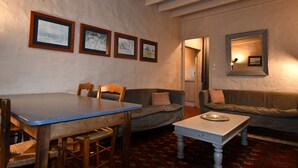 A room with a dining table, two wooden chairs, a sofa, and a small white table. There are four framed pictures on the wall. - Ground level two-bedroom gîte with gated yard. Ideal for young families. (SOYAUX)