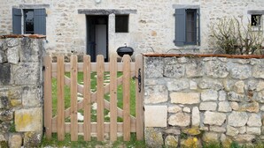 A stone building with a wooden gate, a door, and two windows with shutters. - Ground level two-bedroom gîte with gated yard. Ideal for young families. (SOYAUX)