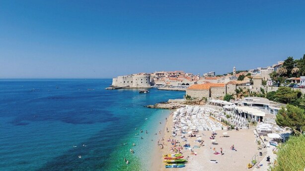 Un pueblo costero con playa, aguas azul turquesa y edificios históricos.