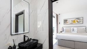Un baño moderno con un lavabo de mármol negro, un espejo grande y un jarrón negro con flores blancas.