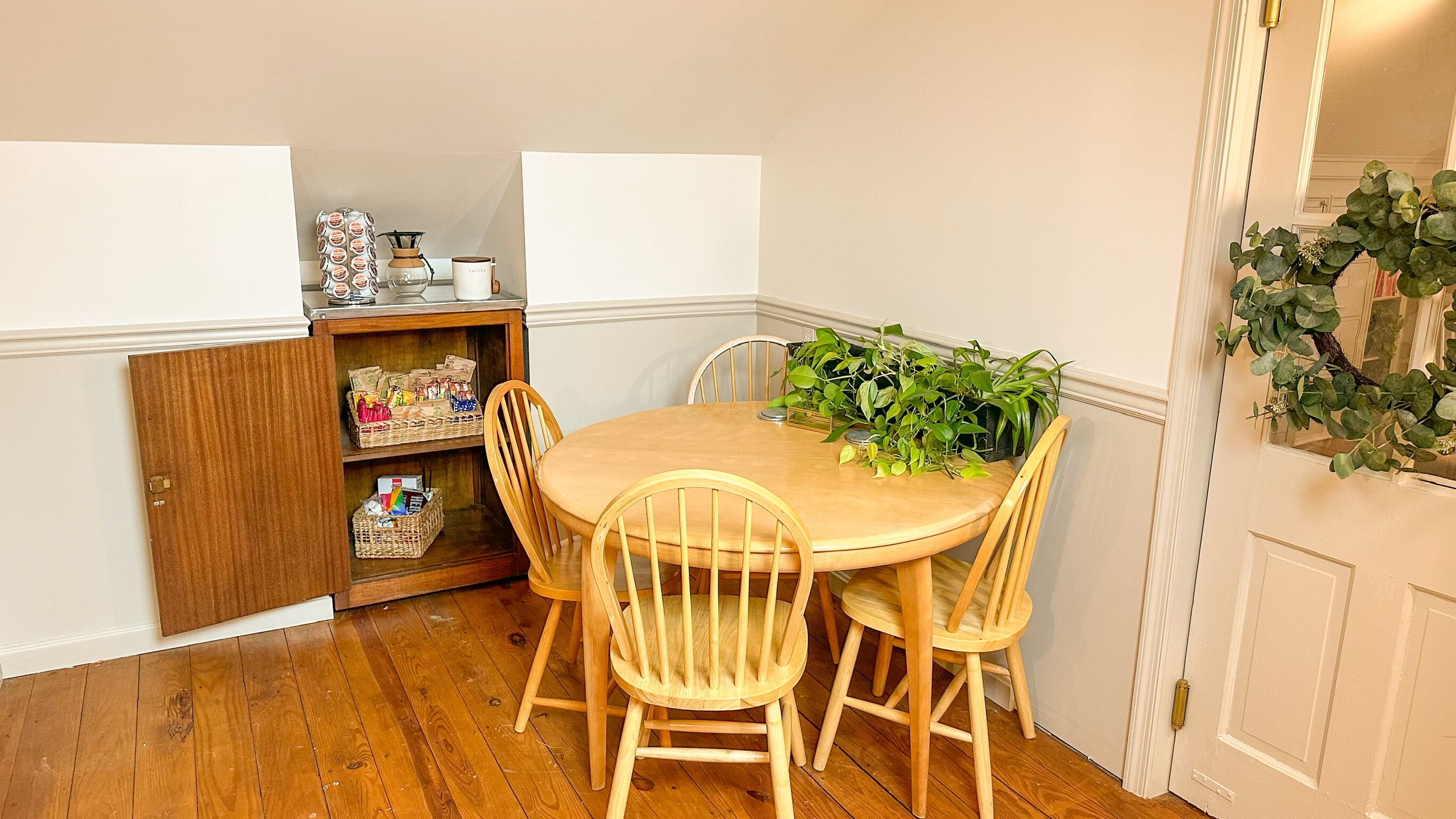Un coin repas avec une table en bois et quatre chaises, un petit meuble contenant des en-cas et une plante en pot posée sur la table.