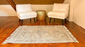 A room with two white armchairs, a round gold table, and a patterned rug on a wooden floor.