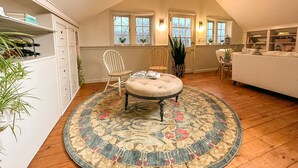 A cozy attic room with a round rug, two chairs, a sofa, and a ceiling fan.