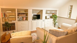 A living room with a sofa, armchairs, a TV, and a bookshelf.