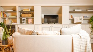 A living room with a sofa, a television, and shelves with books and decorative items.