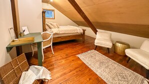 A small, cozy attic bedroom with a sloped ceiling, a wooden bed, a desk, a chair, and a small rug.