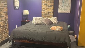 Ein Schlafzimmer mit einem Bett, einem Nachttisch, einer Lampe und einer Ziegelwand.