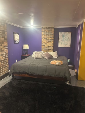 Una camera da letto con un letto, un comodino, una lampada e una parete in mattoni.