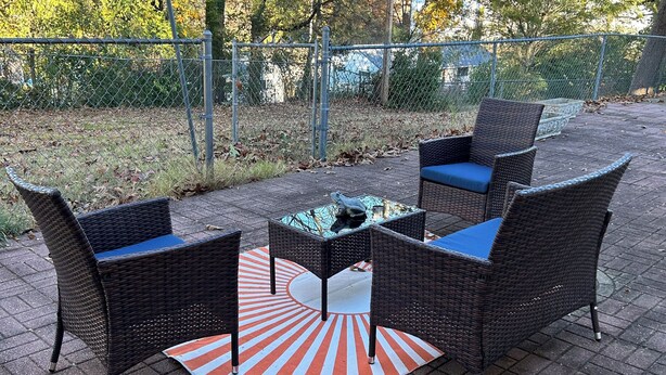 Ein möblierter Patio-Bereich im Freien mit Korbmöbeln und einem gemusterten Teppich.
