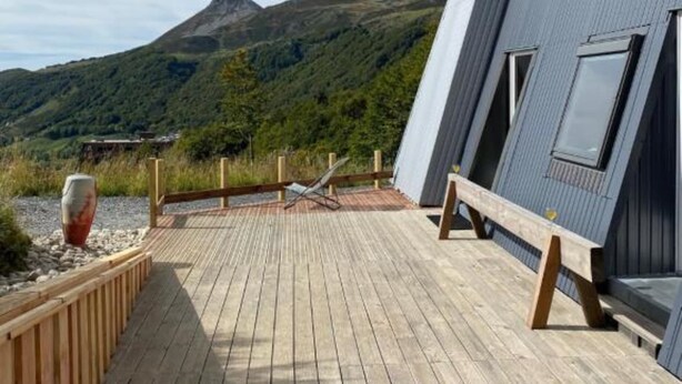Une terrasse en bois offrant une vue sur une montagne et un bâtiment moderne doté de grandes fenêtres.