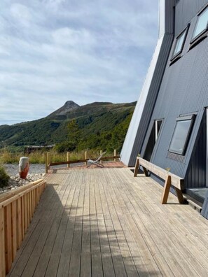 Een houten terras met uitzicht op een berg en een modern gebouw met grote ramen.