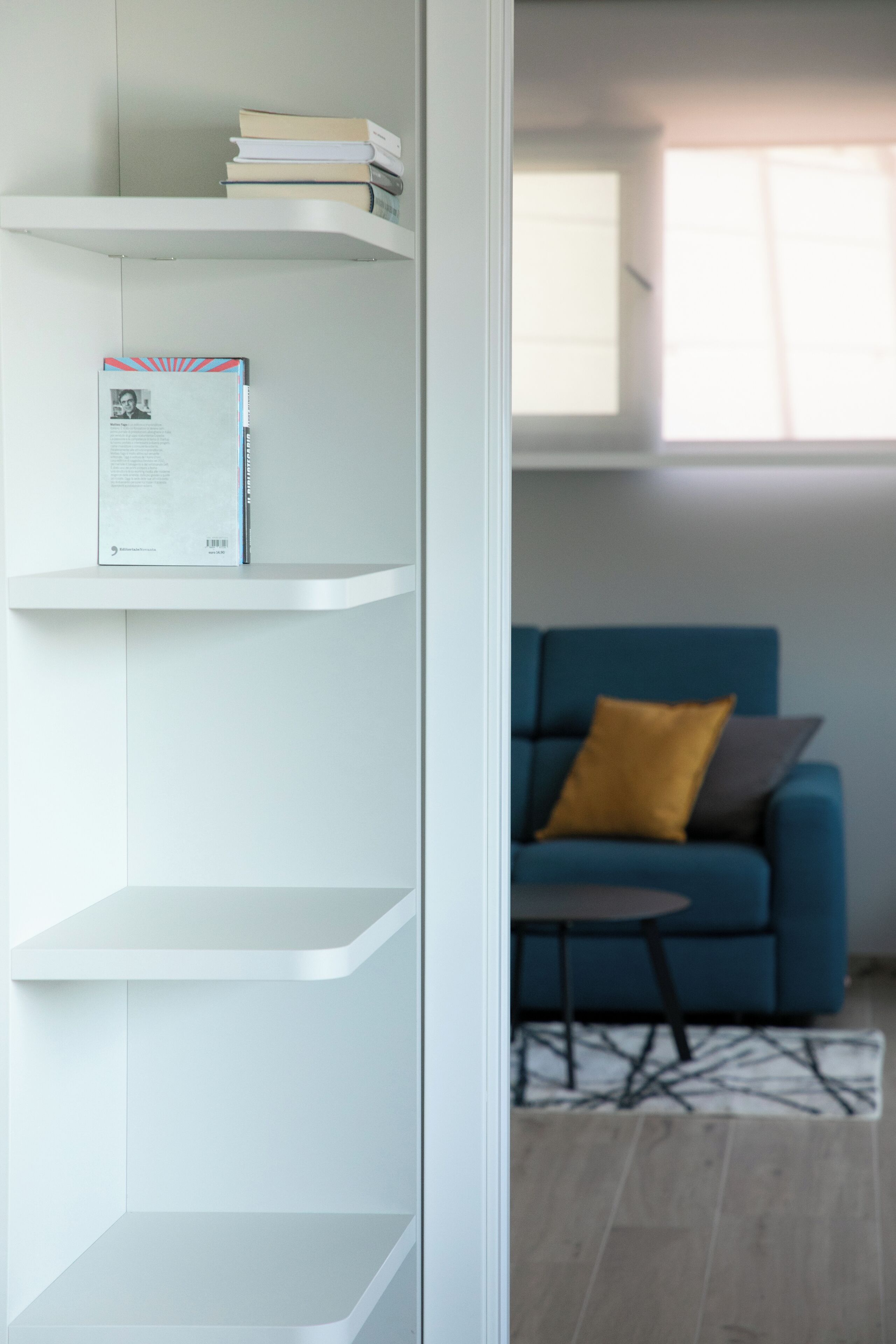 Un intérieur moderne avec des étagères blanches, un canapé bleu agrémenté de coussins et une petite table ronde.