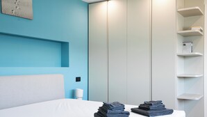 A neatly made bed with folded towels, a white headboard, a blue accent wall, and a white wardrobe.