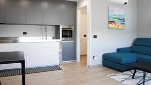 A modern kitchen with grey cabinets and stainless steel appliances, a blue sofa, and a painting on the wall.