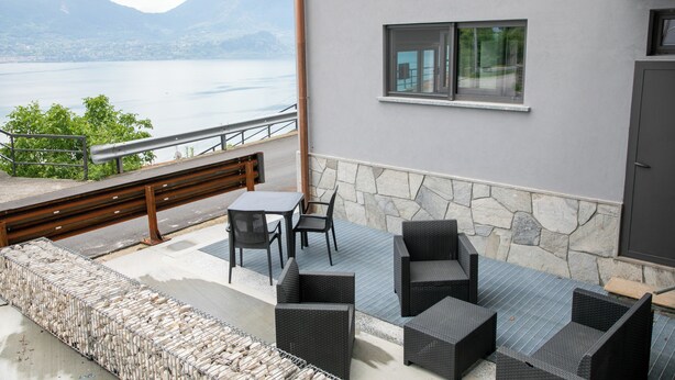 A balcony with outdoor furniture, a stone wall, and a view of a lake and mountains.