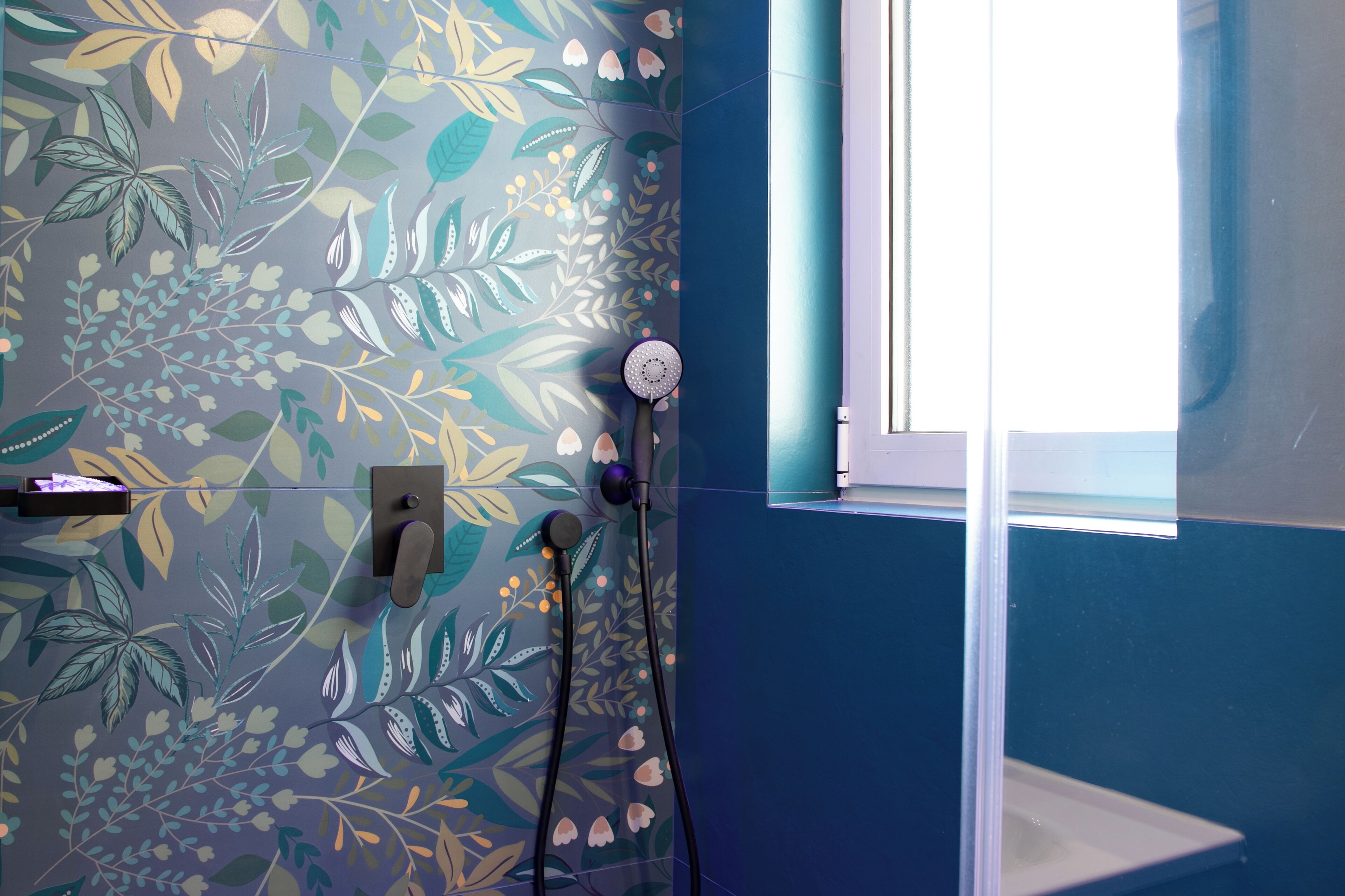 A bathroom with a floral wall design, a window, and a shower area.