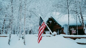 Un chalet enneigé, orné d’un drapeau américain, entouré d’arbres.