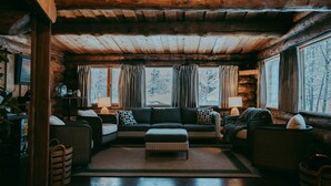 L’intérieur d’une cabane en rondins, avec un canapé, un pouf, des fauteuils en osier et une cheminée.