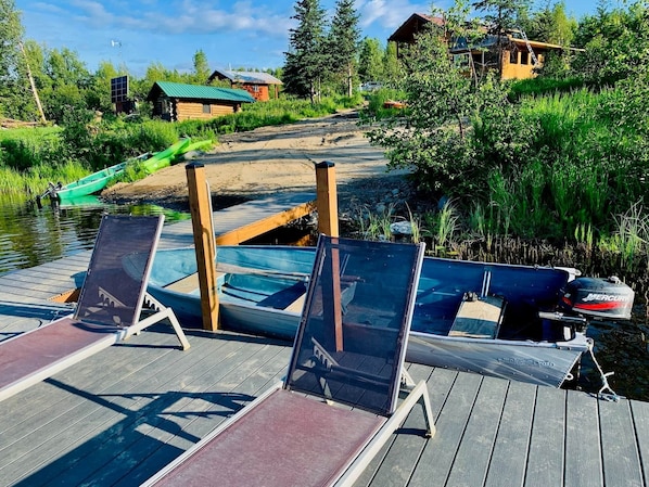 A wooden dock with several boats, a green boat, and a cabin in the background.
