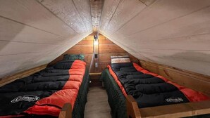 Ein kleines Schlafzimmer im Dachgeschoss mit zwei Betten, Holzwänden und einer geneigten Decke.