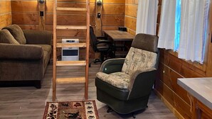 Ein gemütliches Blockhaus-Interieur mit einem Etagenbett, einer Couch, einem Sessel, einem Schreibtisch und einem Esstisch.