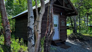 Eine kleine Holzhütte mit einer Tür und einem Schild mit der Aufschrift 'Primitive Cabin #4 Rapha' in einem bewaldeten Gebiet.