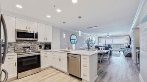 A modern kitchen with stainless steel appliances, a dishwasher, and a large island with a sink. - Seagate 401—Gulf-Front Corner Condo w/ Wraparound Balcony, Pool Access & Sunset Views (Indian Shores)