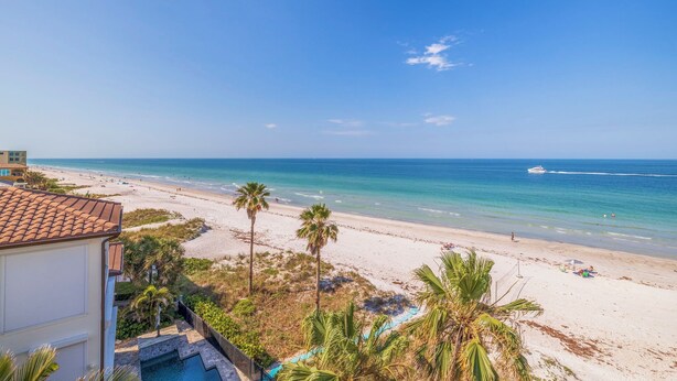 A beach view with a clear sky, a swimming pool, and a building with a tiled roof. - Seagate 401—Gulf-Front Corner Condo w/ Wraparound Balcony, Pool Access & Sunset Views (Indian Shores)