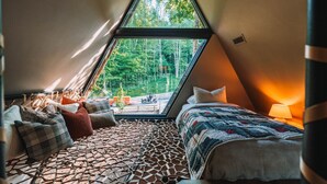 A cozy, triangular bedroom with a large window, a bed, and a seating area with cushions. - The UtopiA @ Paradise Lake (New Philadelphia)