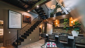 A modern kitchen with a wooden staircase, bar seating, and a large potted plant. - The UtopiA @ Paradise Lake (New Philadelphia)