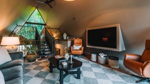 A cozy living room with a checkered floor, a large TV, leather chairs, a staircase with a geometric wall, and a ceiling fan. - The UtopiA @ Paradise Lake (New Philadelphia)