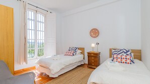 A bedroom with two beds, a chair, a nightstand, and a window with curtains.