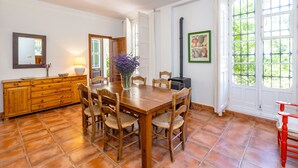 A dining area with a wooden table, four chairs, a vase with flowers, a wooden cabinet, a wall-mounted mirror, and a framed picture.