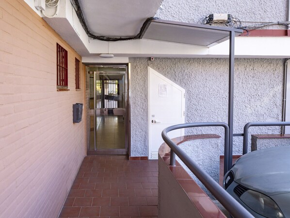 Un pasillo con piso de baldosas, baranda de metal y una puerta que da a una habitación con pared de azulejos.